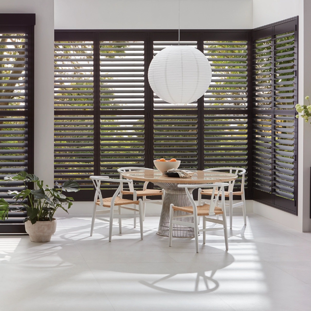 Kitchen with dark wood shutters, round lighting fixture above table and chairs, shutters are tilted open